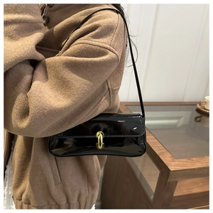 Close-up of black patent leather baguette bag with gold buckle on shoulder