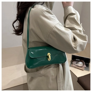 Model wearing a glossy green patent leather baguette bag with a gold metal clasp