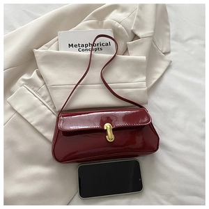 Macro detail of wine red patent leather bag with a gold metal clasp and sleek texture