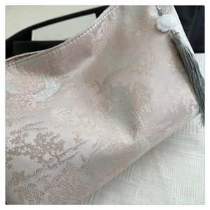 Detailed view of silk brocade fabric with landscape embroidery and lotus tassel charm