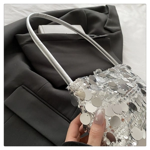 Detailed view of shimmering silver sequin shoulder bag with leather strap on black blazer