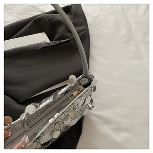 Macro detail of large silver circular sequins and metallic zipper on a fashion handbag