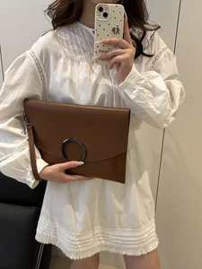 Brown leather envelope clutch bag with metal ring decoration carried by a model