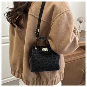 Detail shot of black leopard print crossbody bag with gold twist-lock on a model