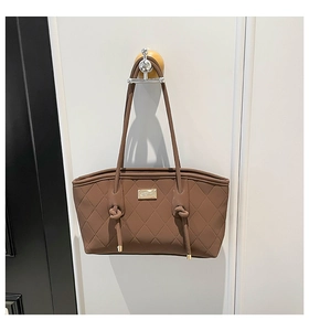 Detail of dark brown quilted tote bag featuring a gold brand plaque and knotted strap hooks