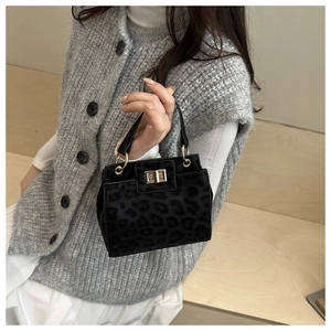 Detail of black leopard print bucket bag with gold clasp held by a model