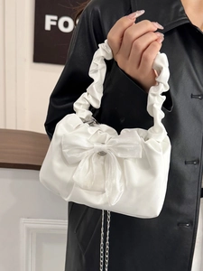 Sac à main blanc plissé avec grand nœud et bandoulière chaîne tenu par un modèle