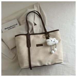 Detail of beige suede tote bag featuring brown straps and a white plush cloud charm