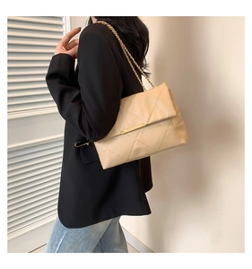 Detail of cream quilted crossbody bag featuring large diamond pattern and gold chain strap