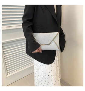 Detail van zilveren pailletten enveloppe clutch met gouden rand vastgehouden door een model