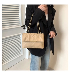 Detail view of khaki quilted crossbody bag with gold chain strap worn by a model