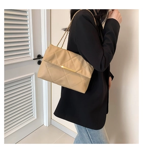 Detail of beige quilted flap shoulder bag with gold chain strap worn on a black blazer