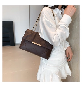 Detail of dark brown quilted crossbody bag with gold chain strap on female model
