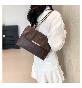 Detail of dark brown quilted crossbody bag with gold chain strap worn by a model