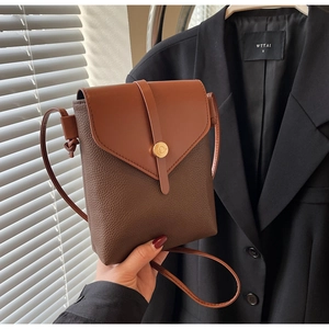 Detail of two-tone brown lychee pattern leather crossbody bag with gold metal buckle