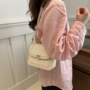 Petit sac à bandoulière beige minimaliste avec boucle dorée sur chemise rose