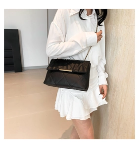 Chic black quilted crossbody bag with gold chain strap worn by a model in a white outfit