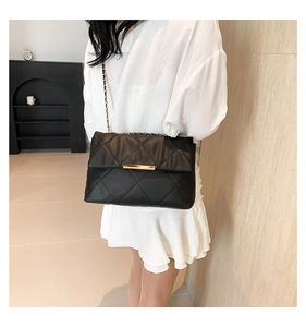 Detail of black quilted shoulder bag featuring gold chain strap and metal lock closure