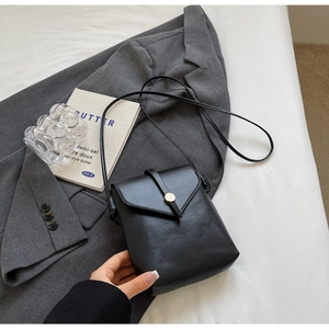 Close-up of black litchi pattern leather crossbody bag with golden hardware on a grey suit