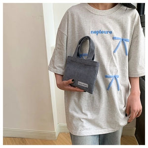 Détail du sac à main en velours côtelé gris foncé avec un t-shirt à nœud papillon bleu