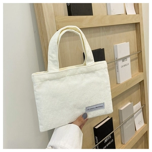 Détail d'un sac cabas en velours côtelé crème avec étiquette sur fond en bois épuré