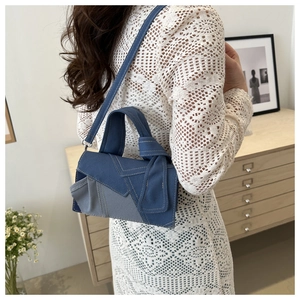 Detail of blue denim crossbody bag with yellow stitching shown on a lace dress