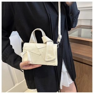 Detail of ivory canvas crossbody bag featuring a knotted handle and geometric flap design
