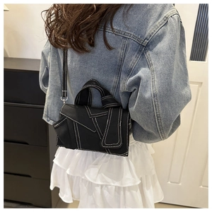 Detail of black crossbody bag with white contrast stitching and deconstructed design