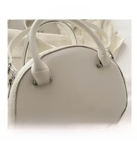 Detail view of white semi-circular leather handbag with silver hardware and dual handles
