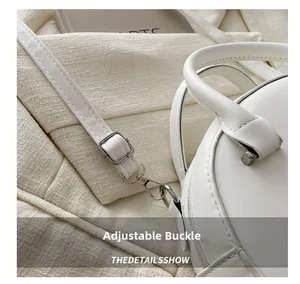 Detail of adjustable metal buckle and leather shoulder strap on white shell handbag