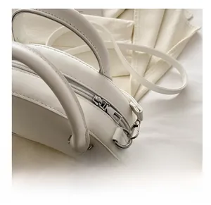 Close-up of smooth silver zipper and round handles on a cream faux leather handbag