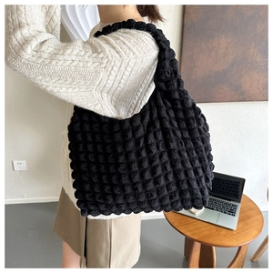 Close-up of black popcorn textured puffy tote bag shown in a casual lifestyle setting