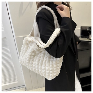Close-up of creamy white bubble textured tote bag worn by a model in a casual indoor setting