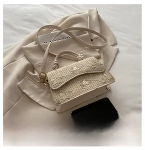 Detail of straw woven crossbody bag featuring floral embroidery and knotted top handle
