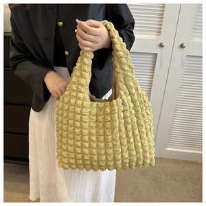 Detail of yellow textured shoulder bag showing pleated fabric and seamless handle design
