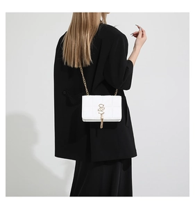 Detail of white quilted leather crossbody bag with gold chain and fringe charm on model