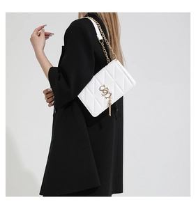Close-up of a white quilted crossbody bag with a gold tassel and metal chain strap