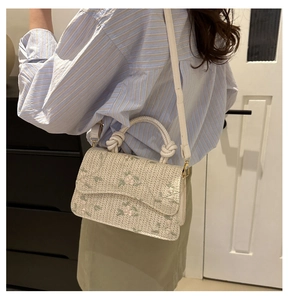 Detail of off-white straw bag featuring delicate pink floral embroidery and woven rope handle