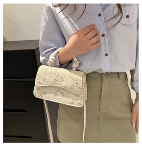 Detail of woven crossbody bag with floral embroidery and unique knotted top handle