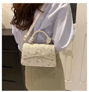 Detail view of woven cream crossbody bag with floral embroidery worn by a model