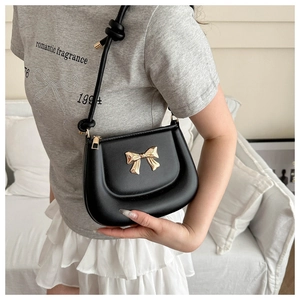 Detail of a black saddle bag with a golden metal bow and stylish knotted leather strap