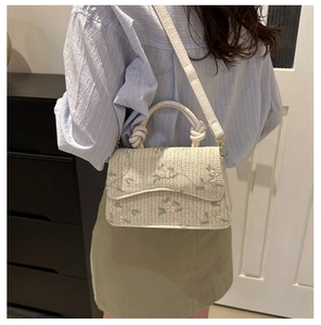 Detail of woven straw handbag featuring pink floral embroidery and creative knotted handle