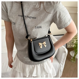Detail of a black leather saddle bag featuring a distinctive golden bow metal clasp