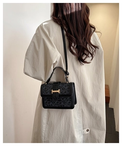Close-up of black crossbody bag with grey monogram print and golden H-shaped clasp