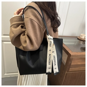 Detail of minimalist black PU leather tote bag with stylish white lettered ribbon strap