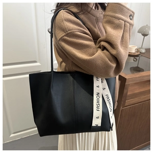 Detail of black tote bag with white decorative lettered webbing strap and matte finish