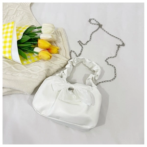Détail d'un sac à main plissé blanc avec grand nœud et bandoulière en chaîne