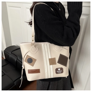 Detail view of large cream tote bag with vintage leather patches worn by a model