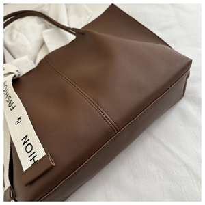 Detail of a brown faux leather tote bag with vertical stitching and logo strap