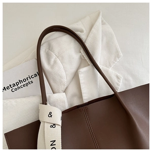 Detail of a brown matte leather tote bag with decorative white ribbon on the handle